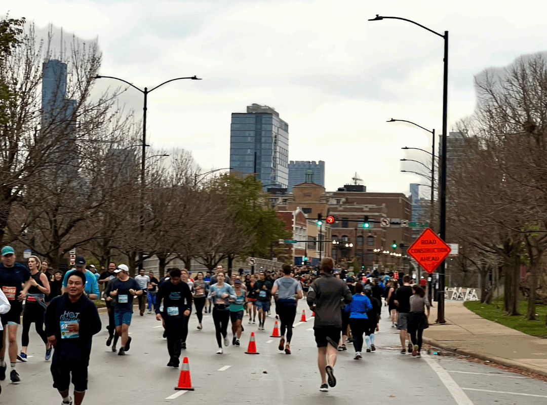 Runners crossing downtown Chicago streets during the 2025 Chicago Marathon with cheering crowds.